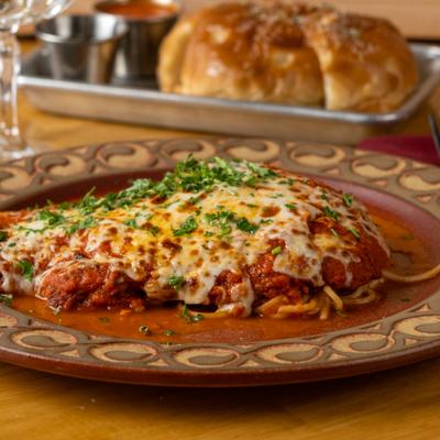 Chicken Parmesan served over pasta with tomato sauce and chopped fresh herbs.