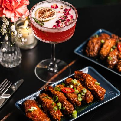 Gazed chicken wings topped with green onions and chili, served with a cocktail.