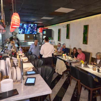 Busy restaurant interior with diners seated at marble tables and bar counter.