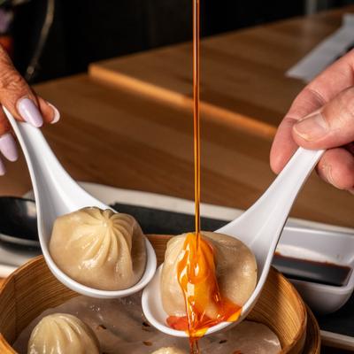 Soup dumpling held in spoons being topped with a sauce.