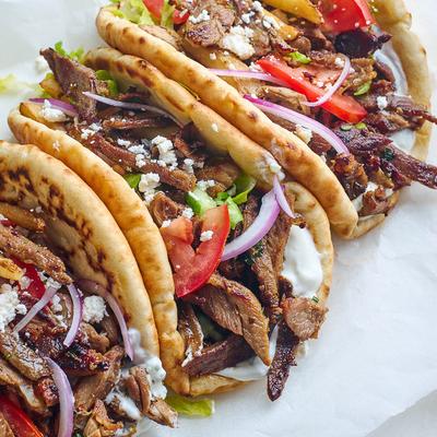 Several gyros topped with onions, tomato slices and cucambers.
