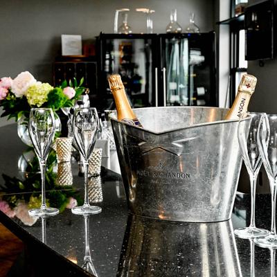 Champagne bottles in an ice bucket on a bar with empty glasses and flowers.