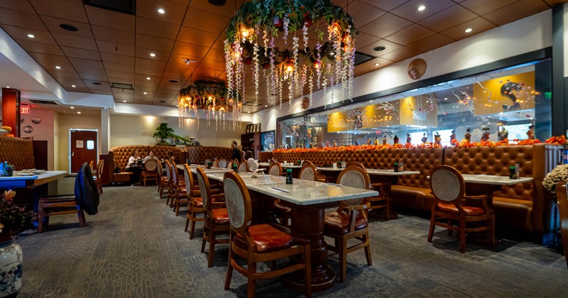 Interior of a restaurant with chandeliers, tables, chairs, and a booth against one wall