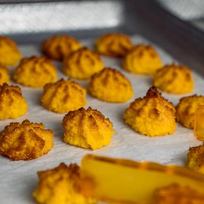 Golden, piped coconut macaroons rest on parchment paper inside a baking sheet.