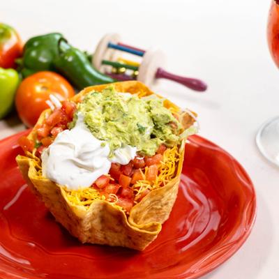 Taco salad with guacamole, tomatoes, sour cream, and cheese in a tortilla bowl.