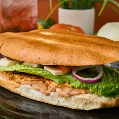 Grilled chicken and steak torta sandwich with lettuce, red onions, and cheese.