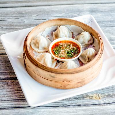 Steamed dumplings in a bamboo basket with dipping sauce.