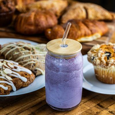 Blanco Smoothie sits on a wooden table, surrounded by a plate of assorted pastries and a muffin.