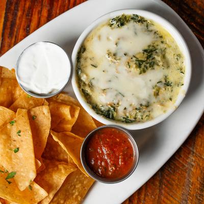 A bowl of spinach dip served with tortilla chips, salsa, and sour cream.