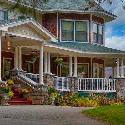 Large country inn with a wraparound porch and autumn landscaping.