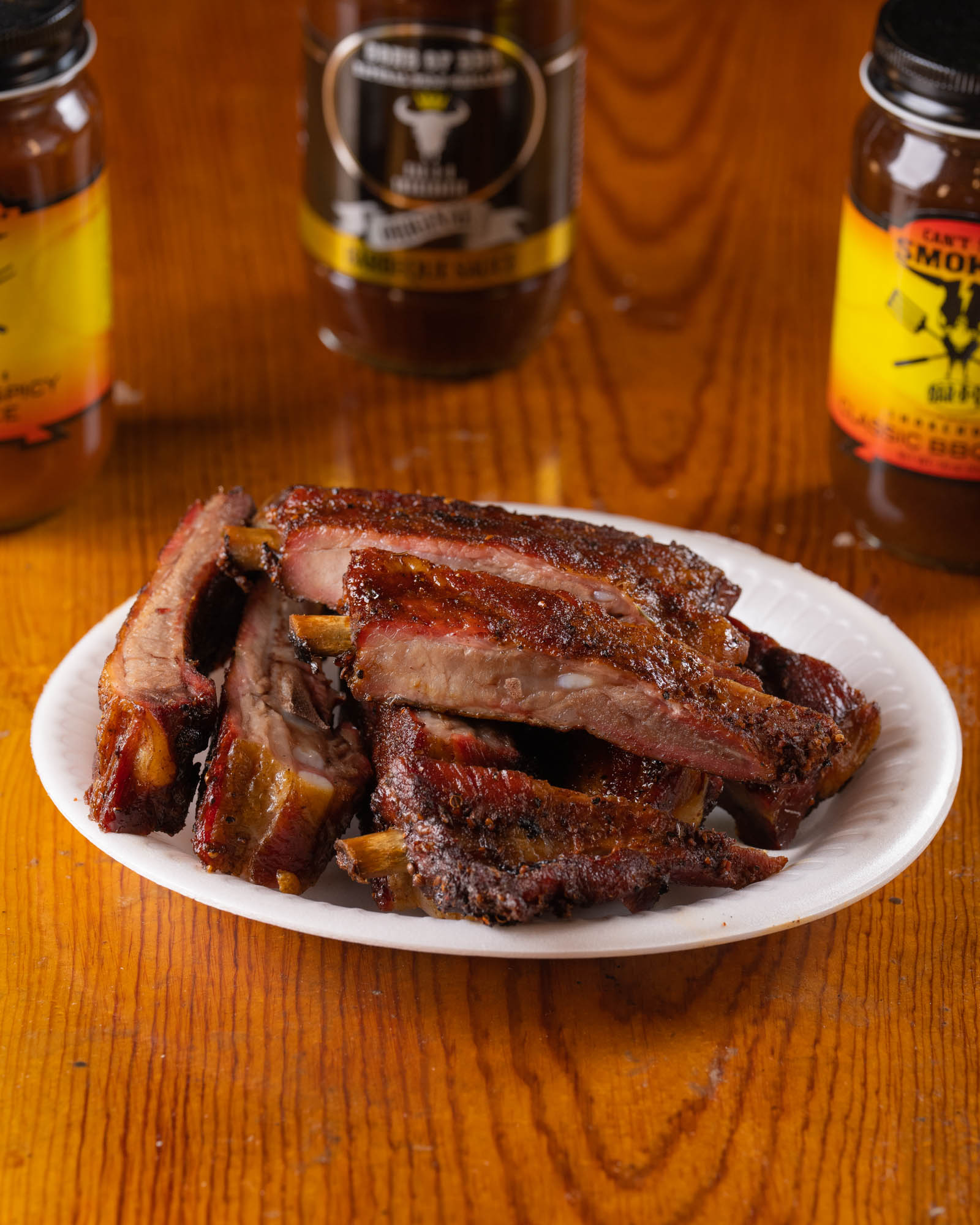 Plate of sliced ribs on a wooden table surrounded by sauce bottles