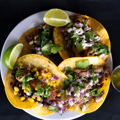 Assorted tacos with various fillings, lime wedges, and a small bowl of green salsa on a white plate.