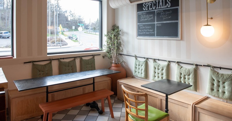 Interior, corner seating area, wooden banquette benches with tables, window, specials board