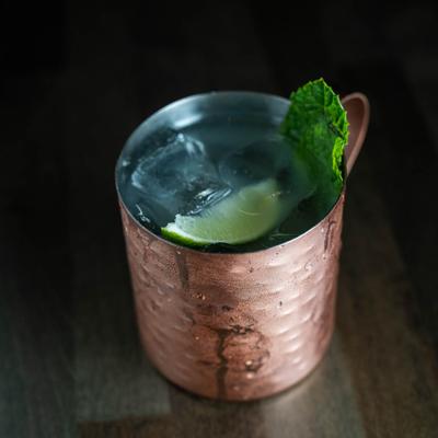 A cocktail drink served in a copper mug, garnished with a mint leaf