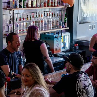 Several patrons are gathered at a bar counter with staff working behind the bar.