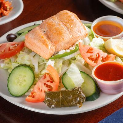 Baked salmon served over a lettuce salad with cucumbers, tomatoes, olives, and dipping sauces.