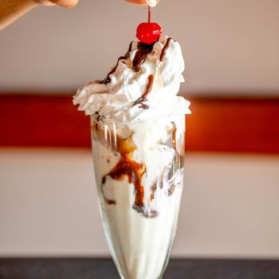 Ice cream sundae topped with whipped cream, chocolate syrup, and a cherry.
