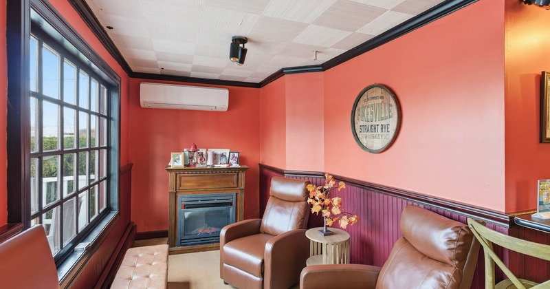 Cozy interior with leather armchairs, fireplace, large window and vibrant orange walls.
