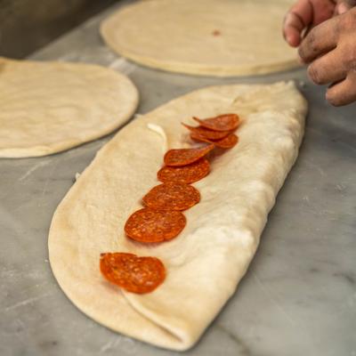 Person preparing a pepperoni pizza.