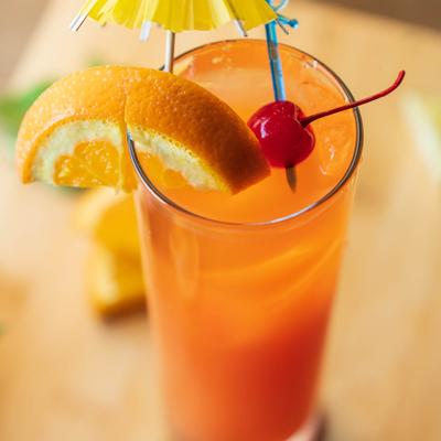 Malibu Sunset cocktail glass garnished with cherry, orange and cocktail umbrella