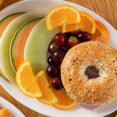 Bagel sandwich served with sliced fruit, along with red grapes.