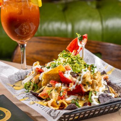 Basket of loaded nachos served alongside a cocktail in wine glass.