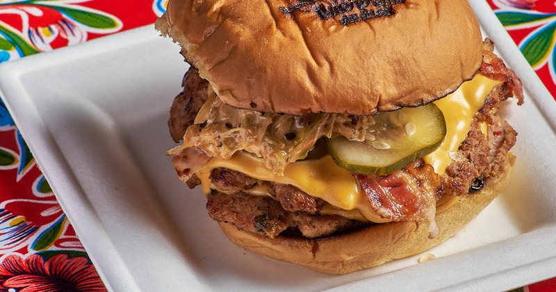 A juicy burger served on a white tray against a vibrant floral tablecloth