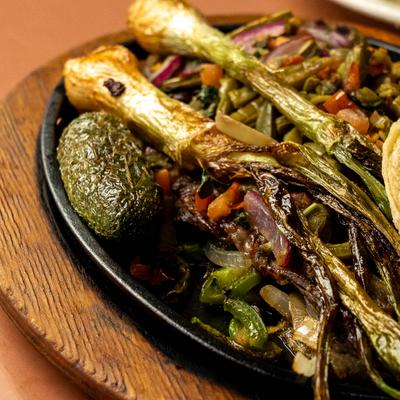 Carne Asada topped with grilled green onions and cactus pad on a cast-iron skillet.