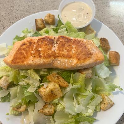 Caesar salad topped with a fillet of salmon , served with sauce on the side.