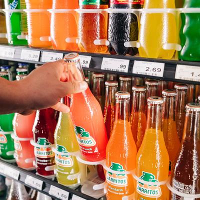 A person takes a Mexican soda bottle from a shelf.