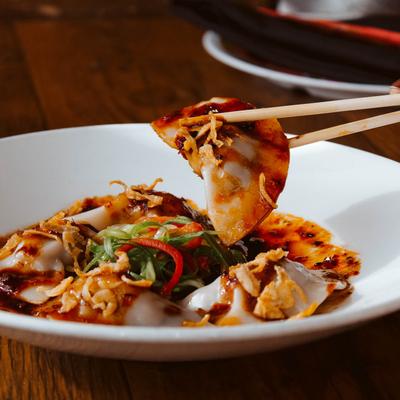 Plate with veggies and dumplings, customer holding some of it with chopsticks.