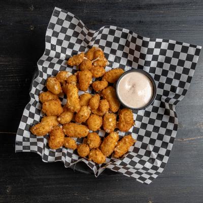 Cheese curds served on a black and white checkered paper with a side of dip.