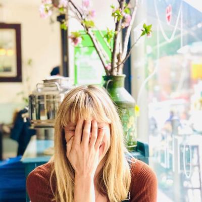 Person sitting by the window indoors, covering face while smiling.
