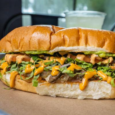Carne asada sandwich topped with avocado and creamy sauce.