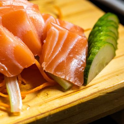 Close up of Salmon Sashimi arranged on a wooden board with shredded carrots and cucumber slices.