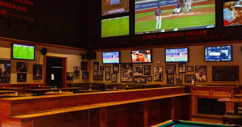 A dimly lit bar with wooden seating and multiple TVs showing sports
