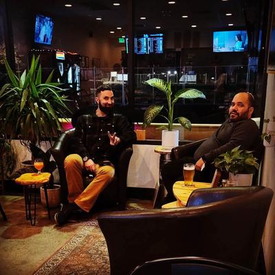 Two guests relax in dark leather armchairs in a lounge setting with house plants.