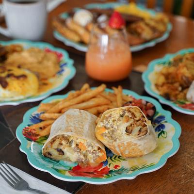 Breakfast burrito served with fries and other other breakfast dishes in the background.