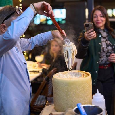 A tableside presentation of pasta being mixed  inside a wheel of Parmigiano-Reggiano cheese.