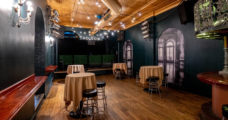 Interior of a stylish venue with string lights, wooden floors, dark walls, round tables with stools