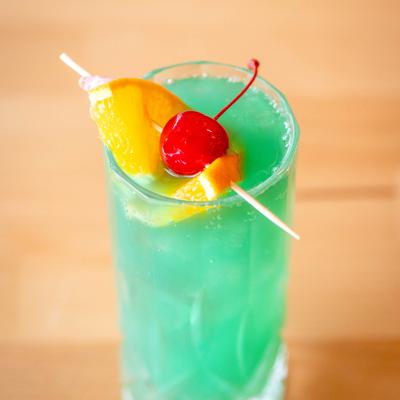 Blue Hawaii cocktail garnished with slice of orange and a cherry.