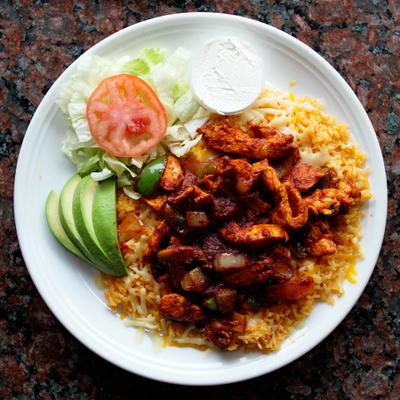 Grilled chicken pieces served over rice with avocado, sour creme and vegetables on the side.