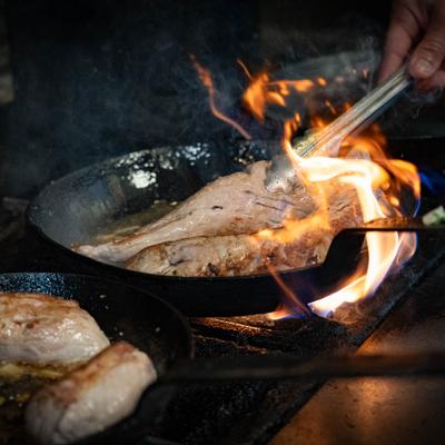 A chef cooking meat over open flame in a pan.