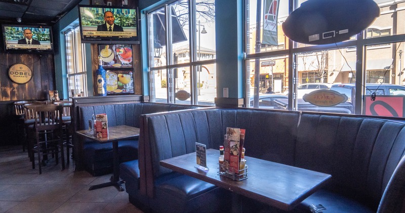 Interior with booth seating, televisions and large windows overlooking a street.