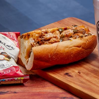 Chicken cheesesteak sandwich beside a bag of chips.