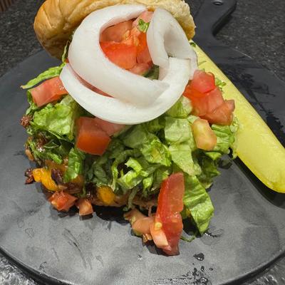 Loaded burger topped with chopped lettuce, diced tomatoes, and raw onion rings.