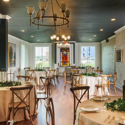 Dining room with round tables, and wooden cross-back chairs and chandeliers.