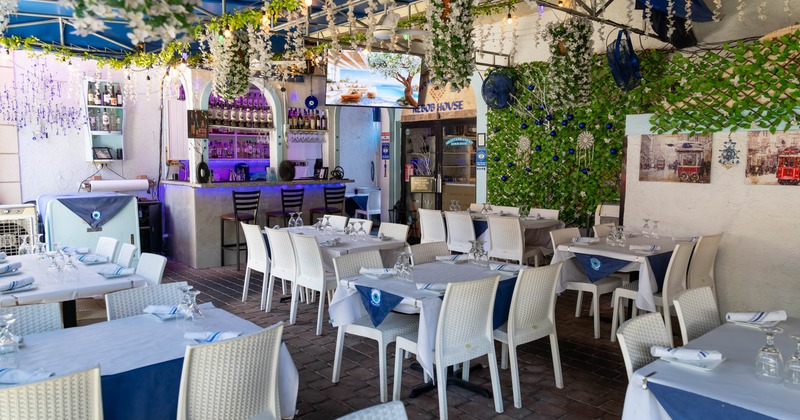 Outdoor restaurant with white tables, a bar area, and decorations of vines and flowers