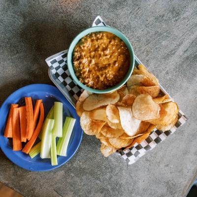 Sloppy Joe dip, served with potato chips, carrot and celery, top view.