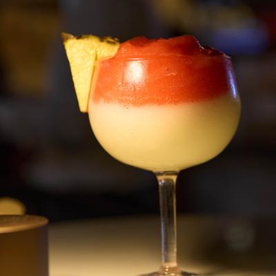 Layered cocktail in coupe glass with pineapple slice.